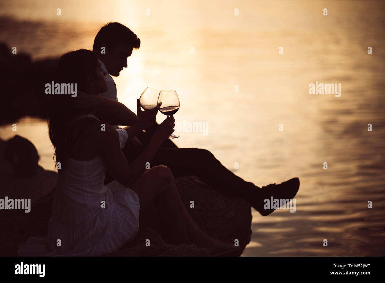 Romantic couple drinking wine at sunset at a pier on a seaside.Romance.Two people having a romantic evening with a glass of wine near the sea.Enjoying Stock Photo