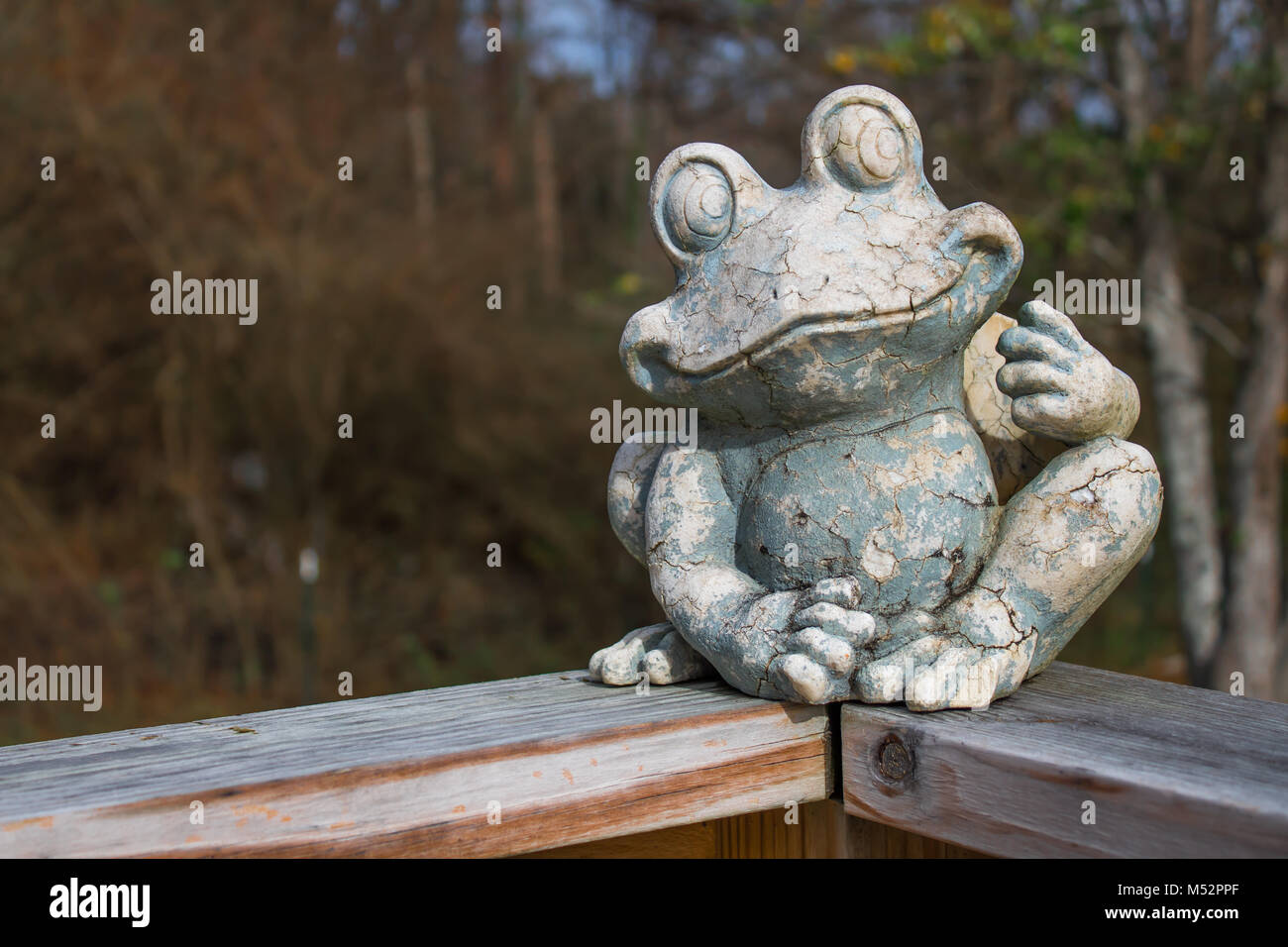 An old rustic frog sculpture sitting on a wooden railing Stock Photo