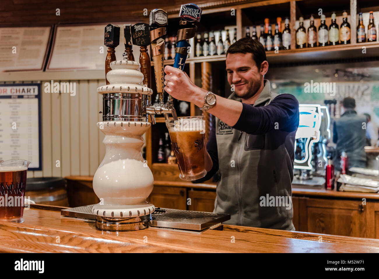 Bartender fills pitcher of beer at tap station well stocked with a variety of Samual Adams brews. The well-known brewery with a long history lures loc Stock Photo
