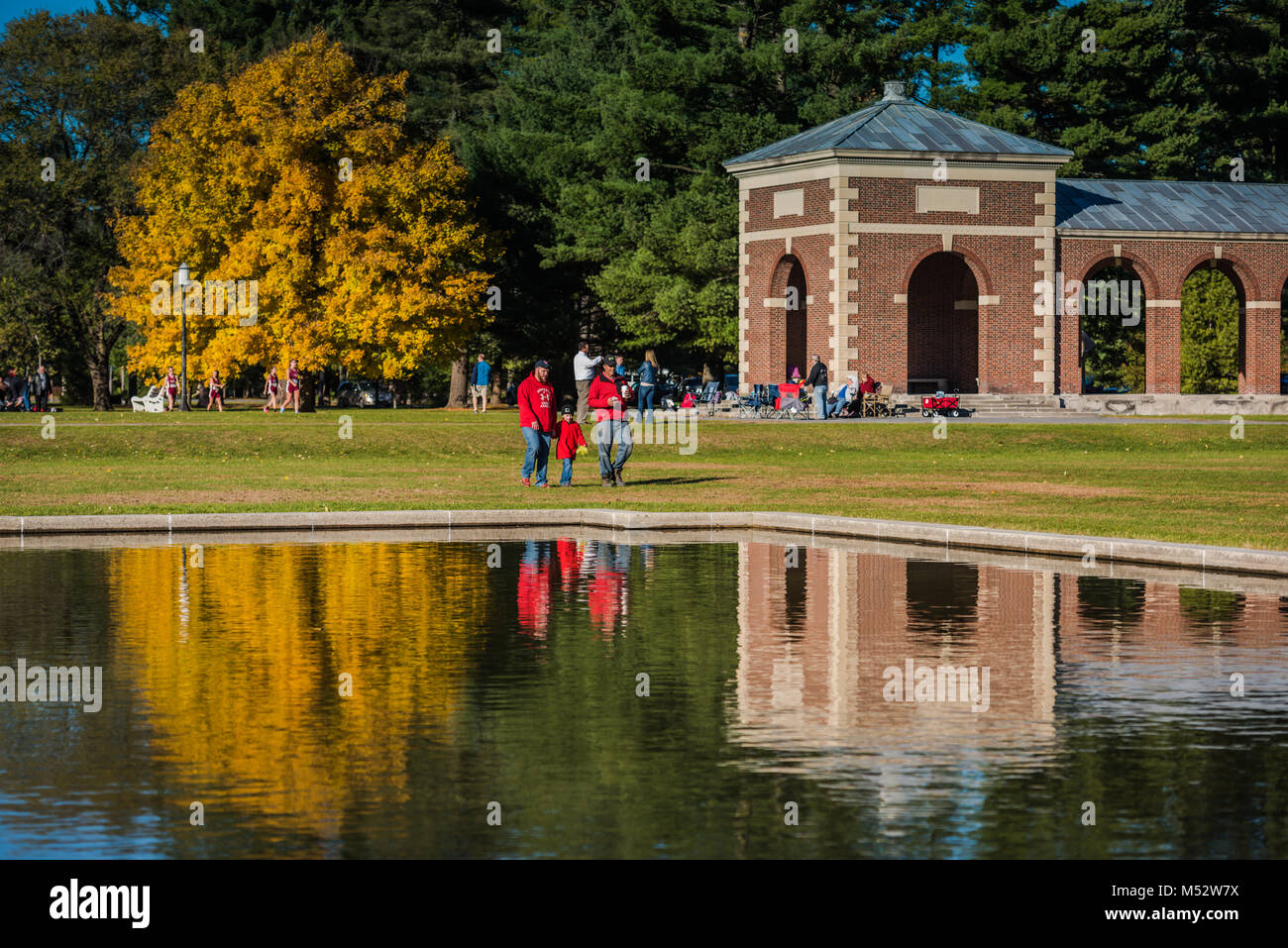 Family walk in the park past fall reflection on pool. Stock Photo