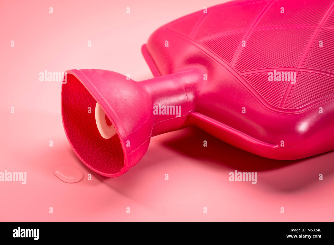 red watter rubber bottle on pink background - heat and cold therapy Stock Photo