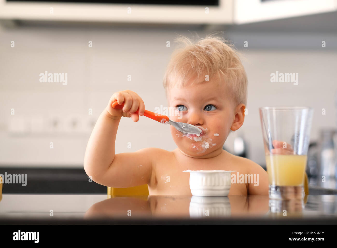 Adorable one year old baby boy eating yoghurt with spoon Stock Photo