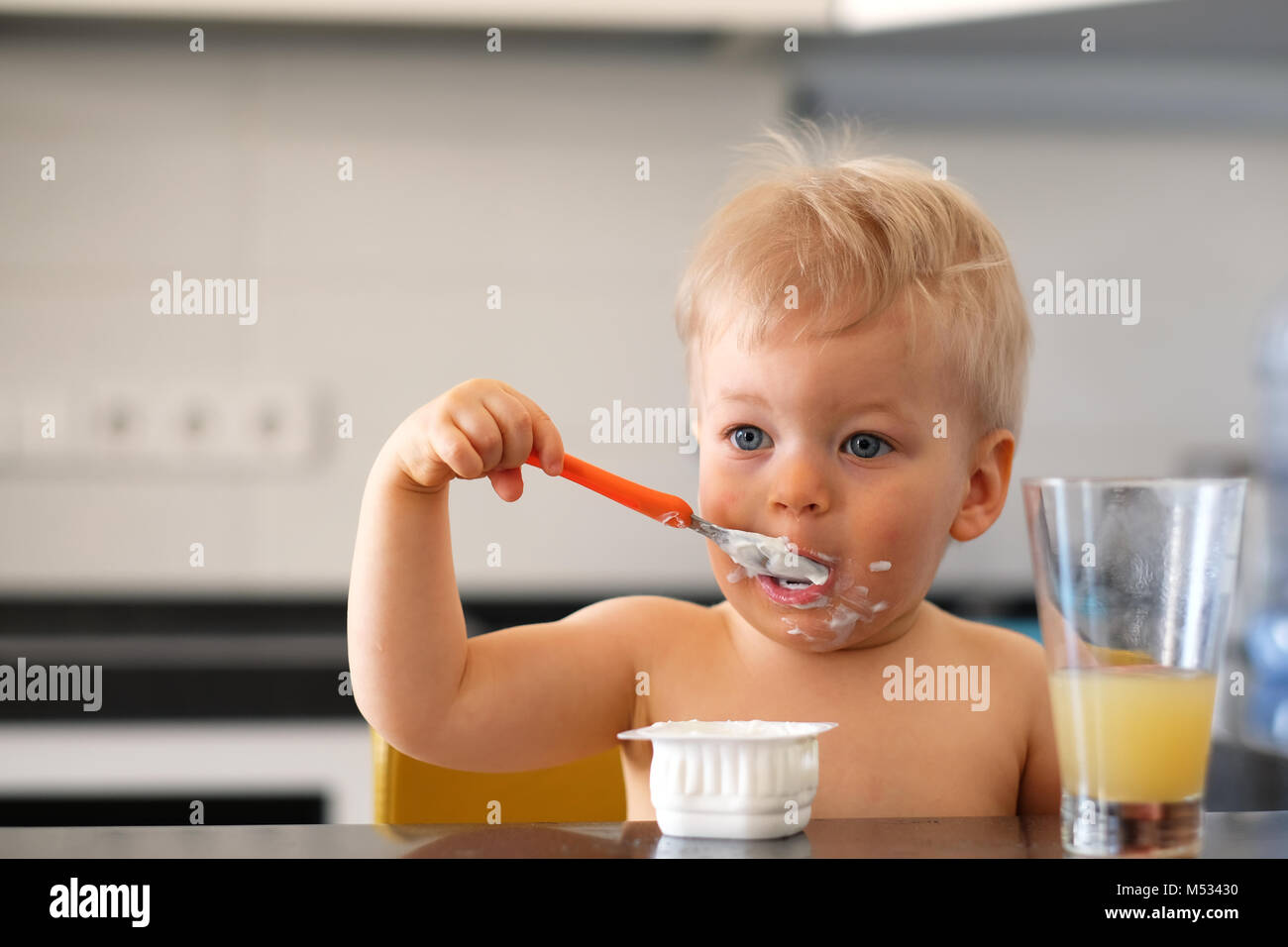 Adorable one year old baby boy eating yoghurt with spoon Stock Photo