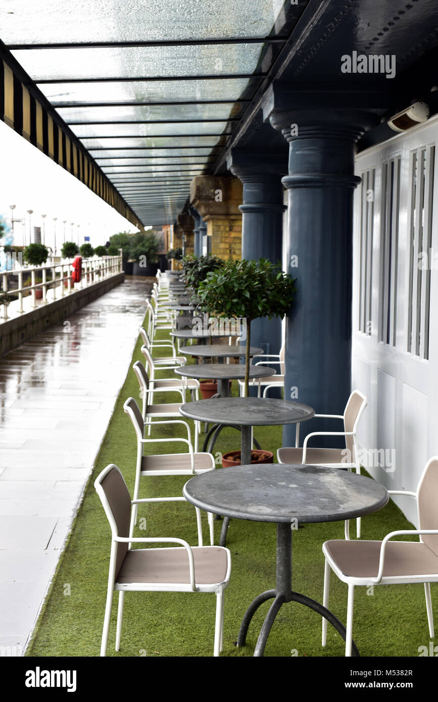 A row or line of tables and chairs on the riverbank of the thames in central london outside of a restaurant or cafe for dining alfresco in the city. Stock Photo