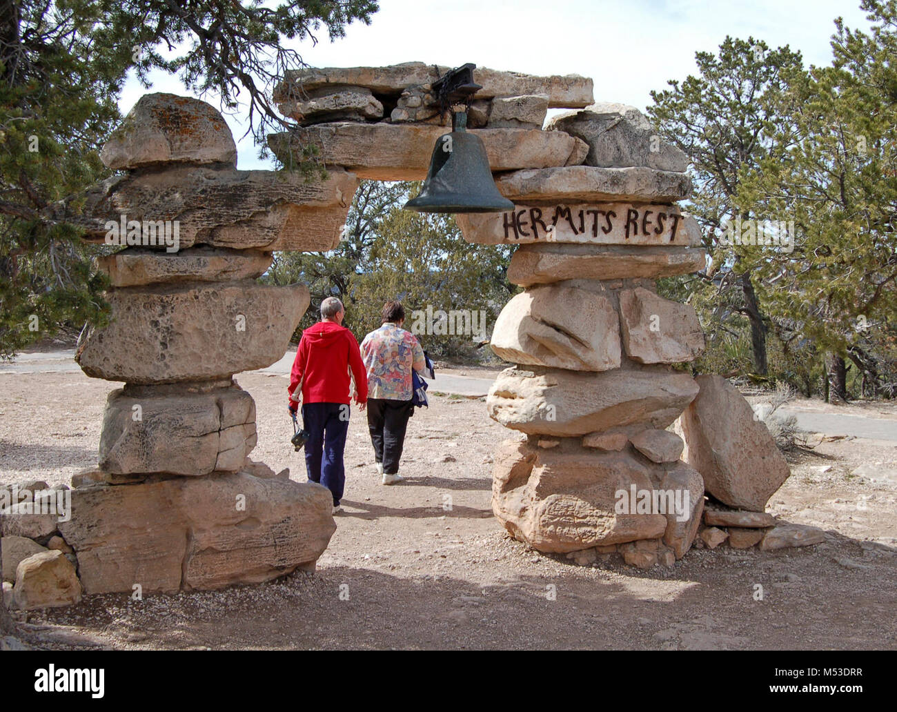 Grand Canyn Hermits Rest Arch & Bell .. The original entrance to Hermits Rest. Mary Colter, one of Grand Canyon's most famous architects, built Hermits Rest in 1914 to look like an old miner's cabin, complete with a giant fireplace and front porch. Today Hermits Rest has a gift shop and small snack bar. Restrooms are available here. The Hermit Trail, winding steeply down into the canyon, begins about 0.5 miles, 0.8 km west of Hermits Stock Photo