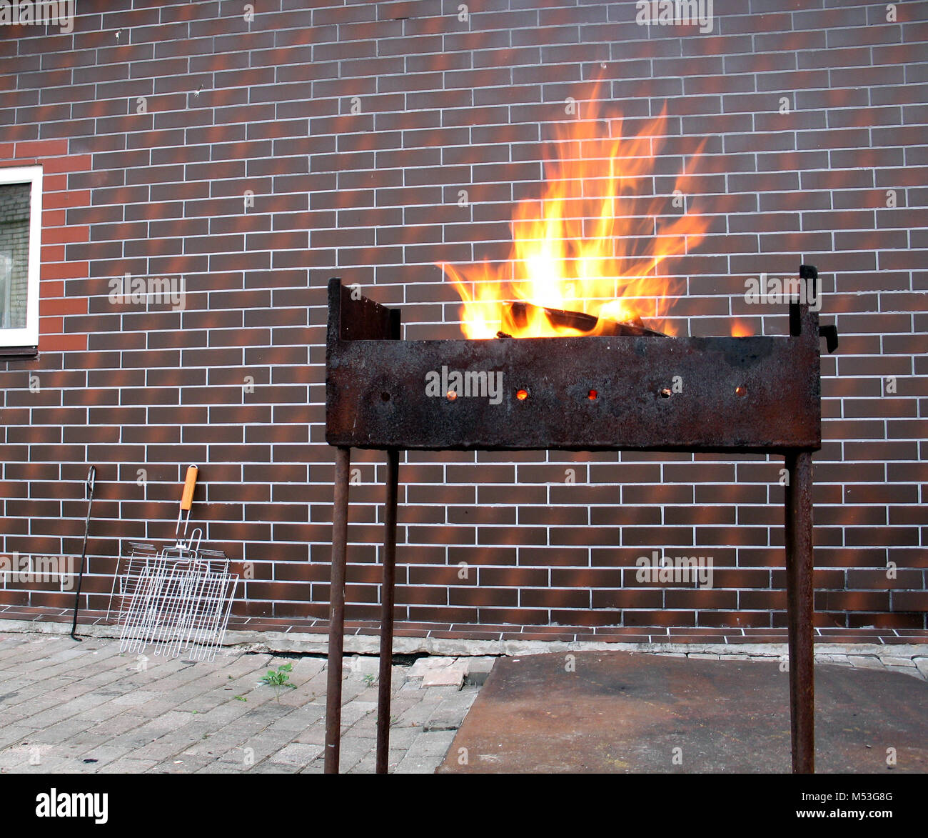Firewood and fire in the old rusty charcoal grill on brick wall background Stock Photo