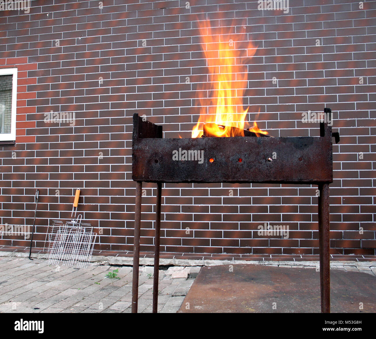 Firewood and fire in the old rusty charcoal grill on brick wall background Stock Photo
