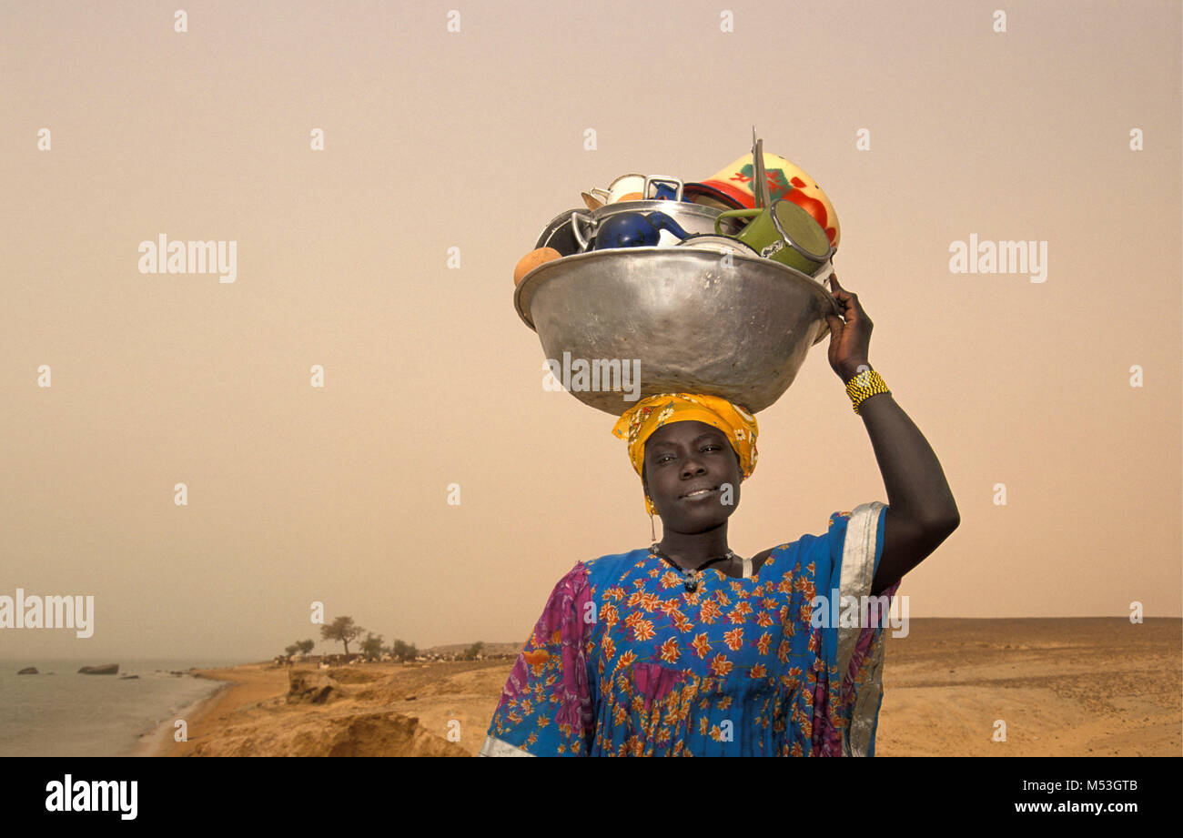 Mali. Timbuktu. Sahara desert. Sahel. Songhai, Songrai tribe. Woman returns home from washing dishes in Niger river, carrying dishes on head. Stock Photo