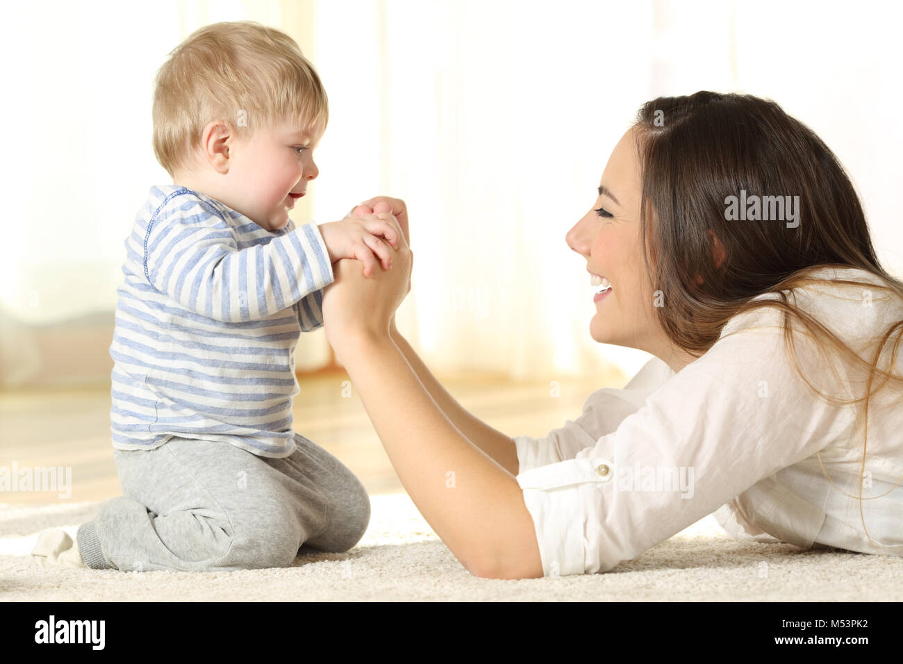 Profile of a happy mother and her kid son holding hands lying on the floor at home Stock Photo