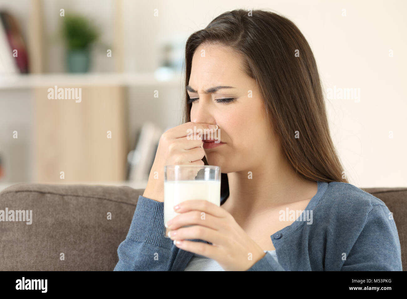 Disgusted woman holding a milk glass with bad odor sitting on a couch in the living room at home Stock Photo