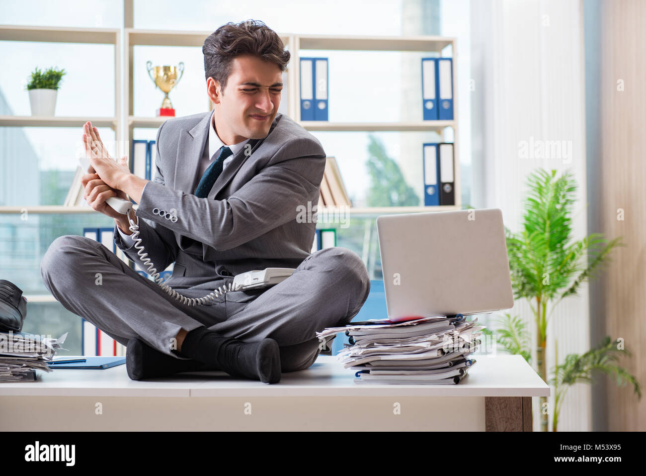Businessman sitting on top of desk in office Stock Photo - Alamy