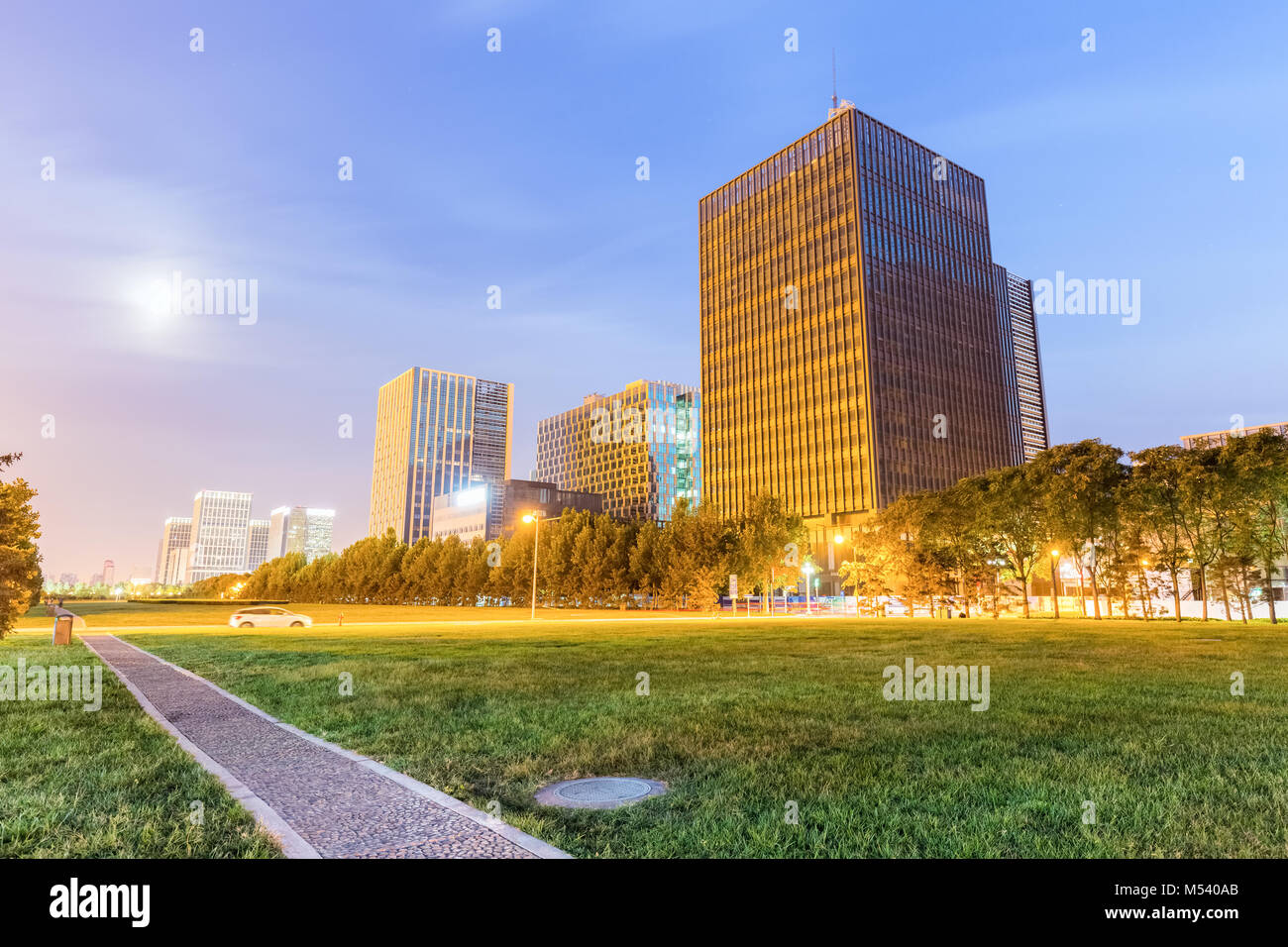 park footpath and lawn with modern buildings at night Stock Photo