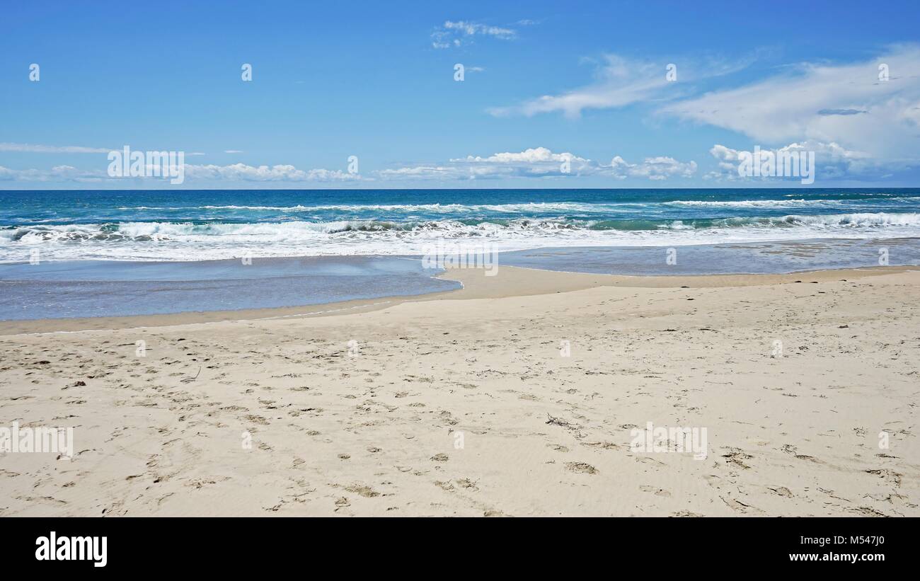 Footprint covered section of beach with ocean waves and blue sky in the background. Stock Photo
