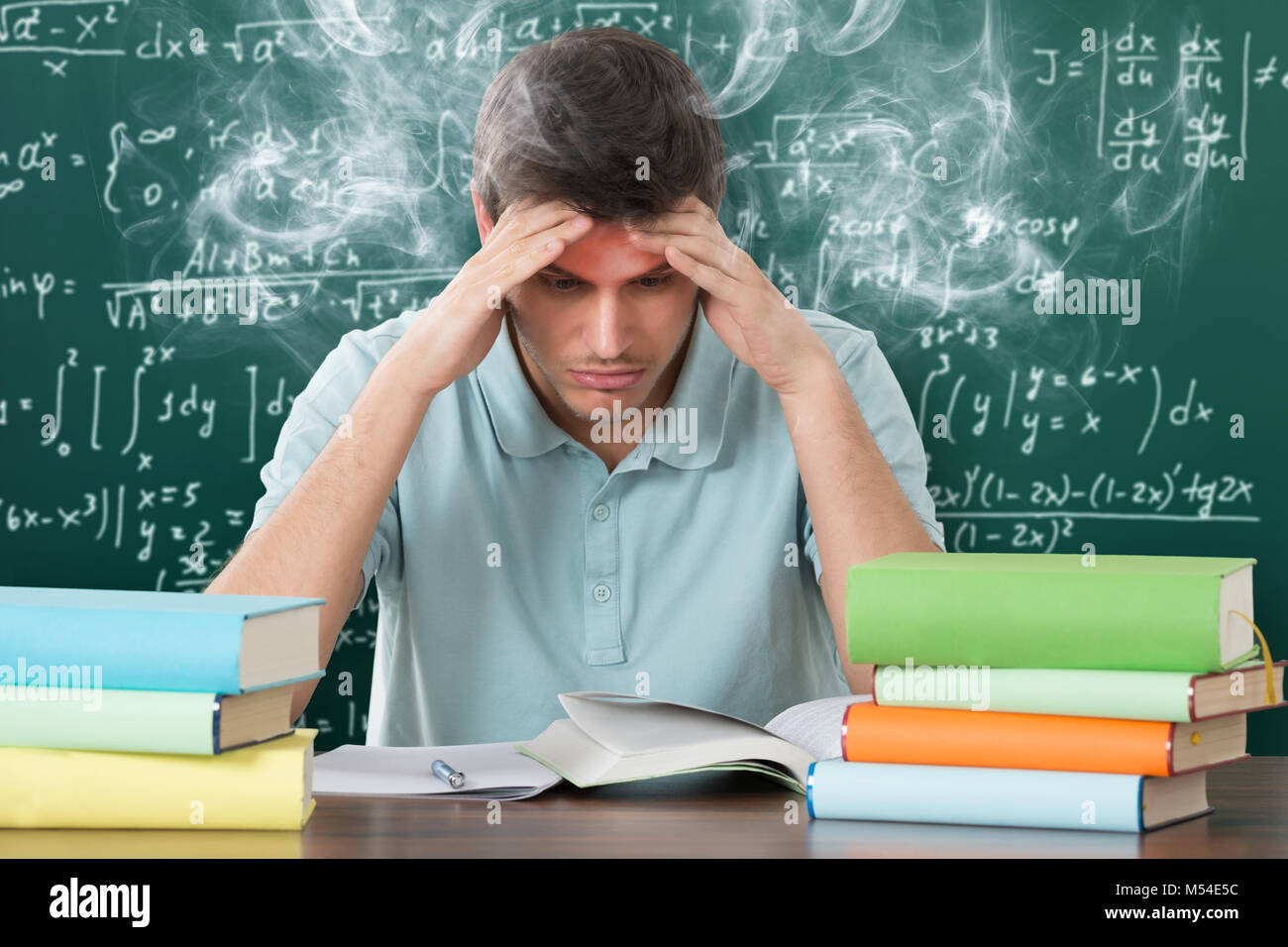 Worried Male Student Looking At Books At Wooden Desk Stock Photo