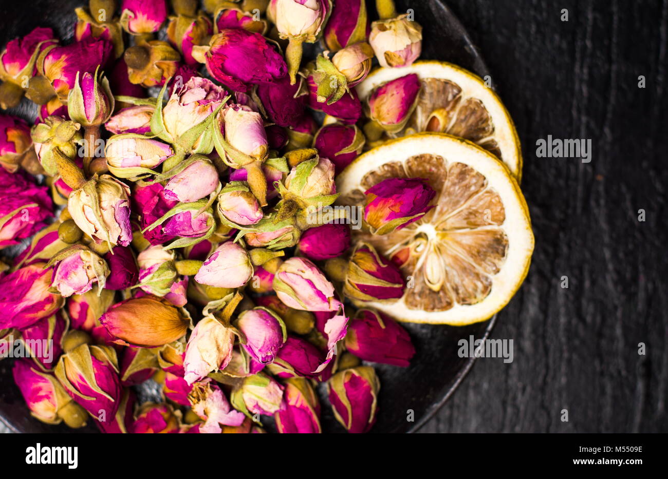 Rose tea buds and lemon slices on dark plate Stock Photo