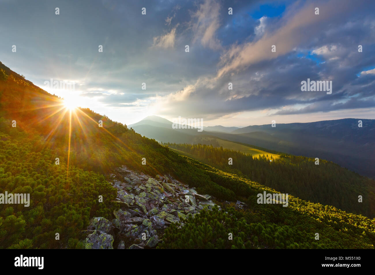 Last sun rays in evening sky with clouds above Syniak mountain. Summer sunset view from Homiak mountain, Gorgany, Carpathian, Ukraine. Some lens flare Stock Photo