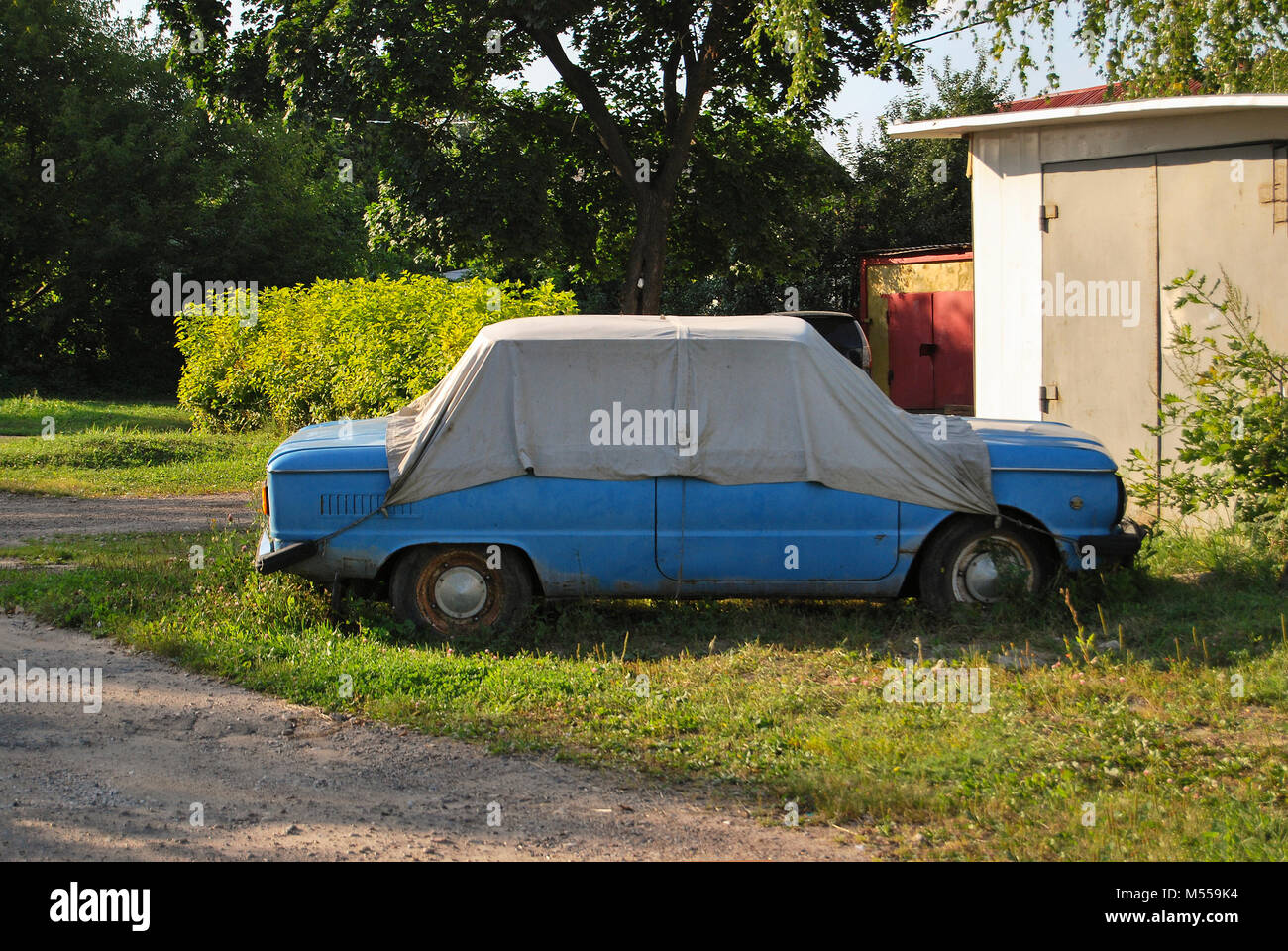 An old rusty Soviet-made ZAZ car, covered with a tent, stands in the village. Stock Photo