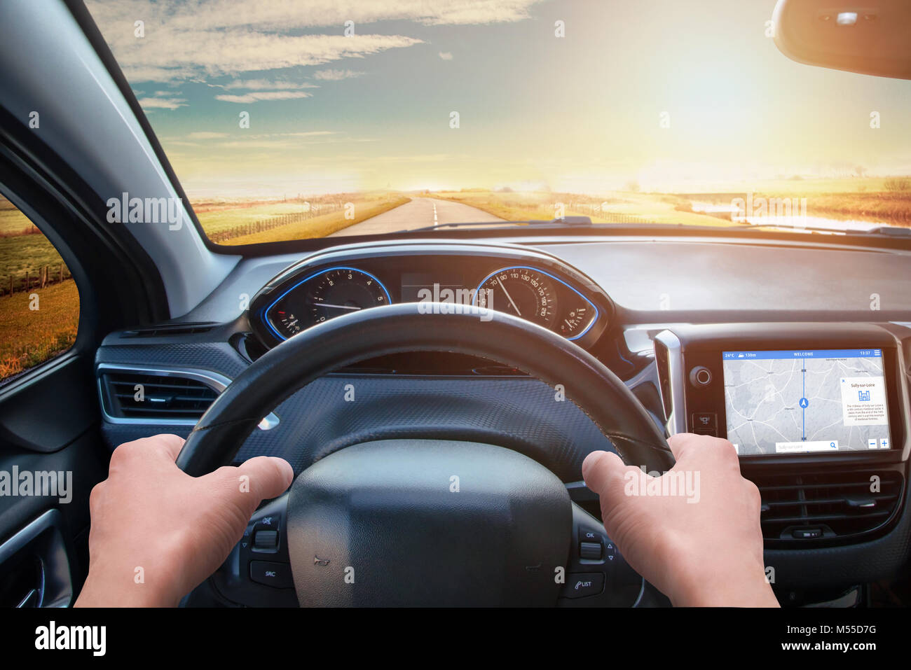 View from the driver's eyes to the steering wheel and the road. Modern car interior with navigation on board display. Stock Photo
