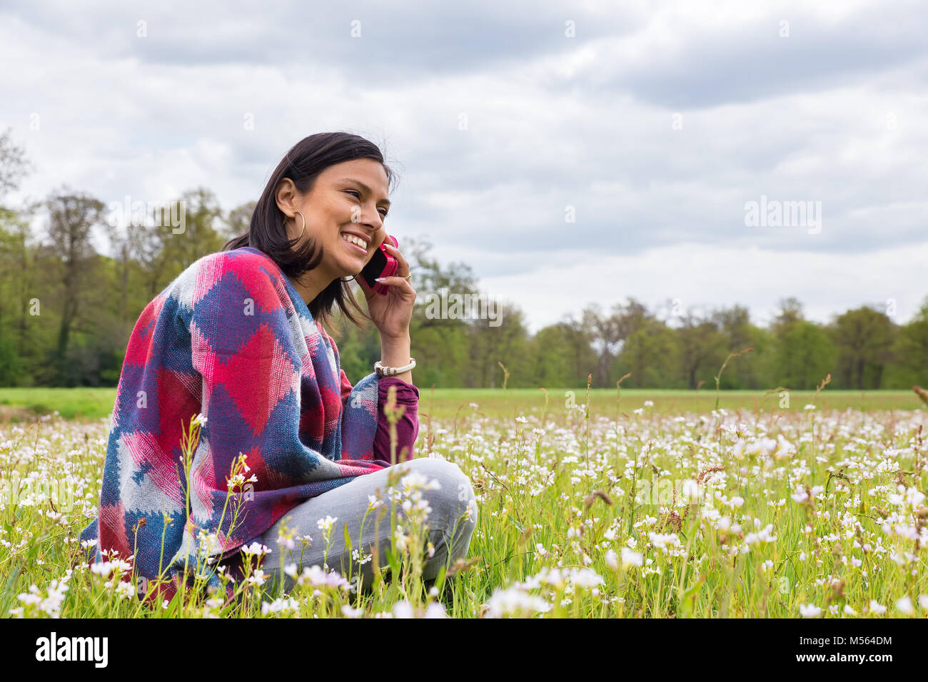 Woman sits in blooming meadow phoning mobile Stock Photo