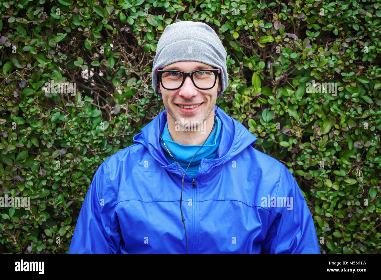 Portrait of handsome young guy in sport clothes against green bush looking at camera and smiling. Stock Photo