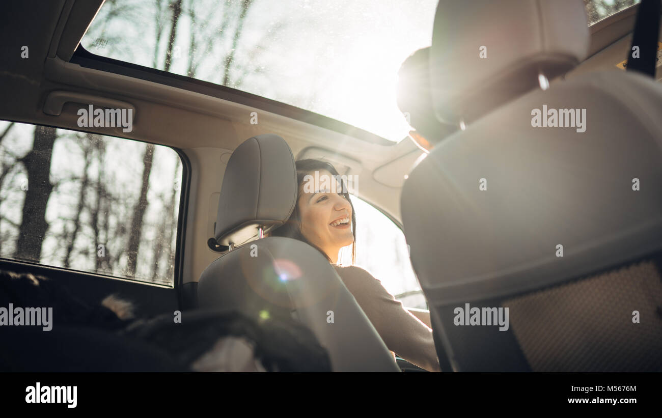 Young woman in a car,female driver looking at the passenger and smiling.Enjoying the ride,traveling,road trip concept.Driver feeling happy and safe.Le Stock Photo