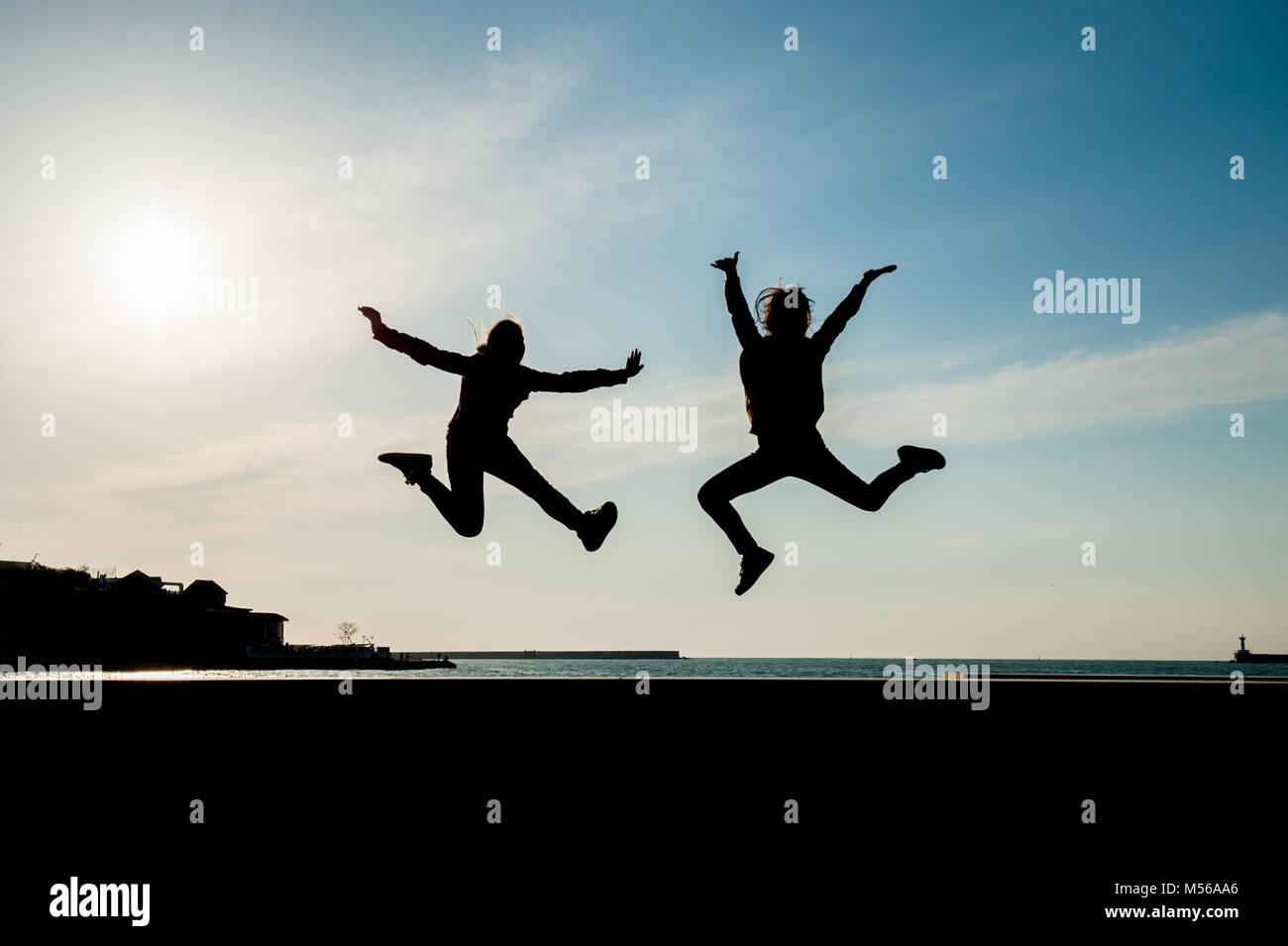 two happy jumping teen girls on blue sky background at sea sunset Stock ...