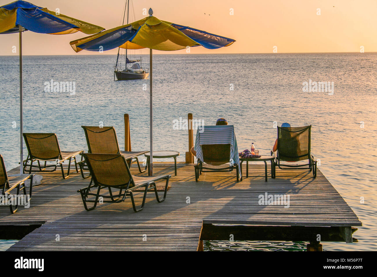 Couple sitting in deckchairs on a wooden boatdeck relaxing and enjoying the sunset in the Carribean Stock Photo