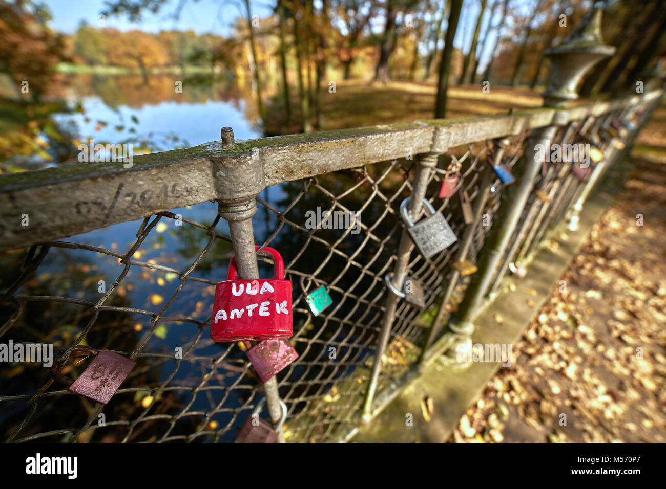 Sunny autumn landscape - park in golden colors, balustrade on the bridge of love decorated with padlocks of couples in love, in the background a pond Stock Photo