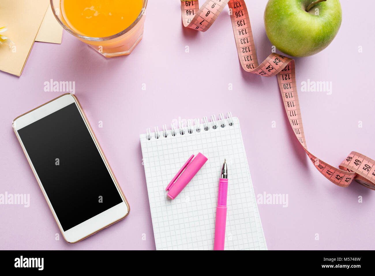 Top view of green apple, measuring tape, mobile phone, pen and open notebook. Fitness Concept