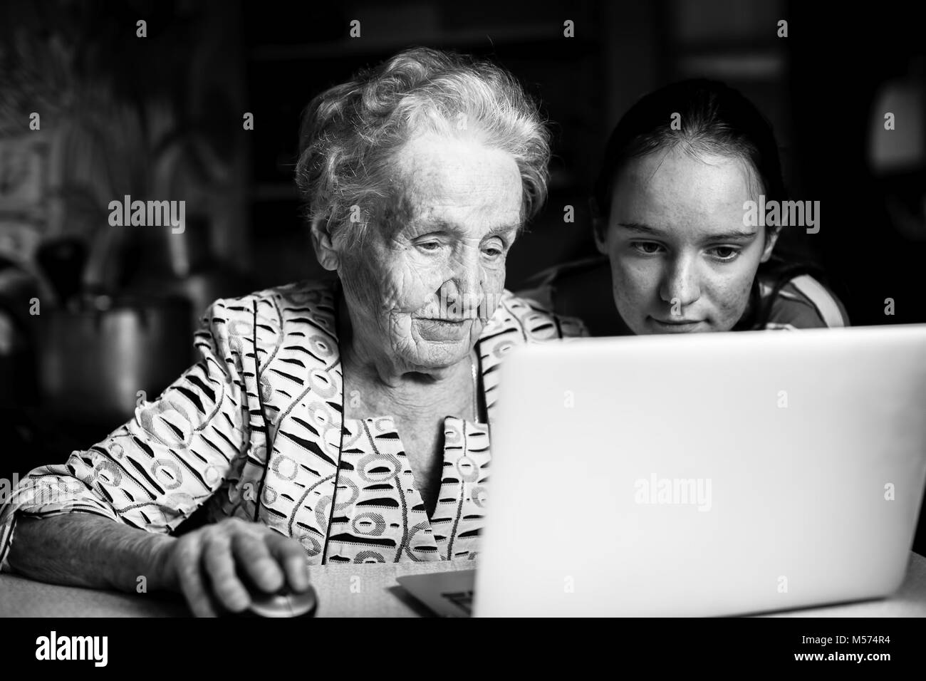 Teen girl teaches her grandmother to type on the laptop. Stock Photo