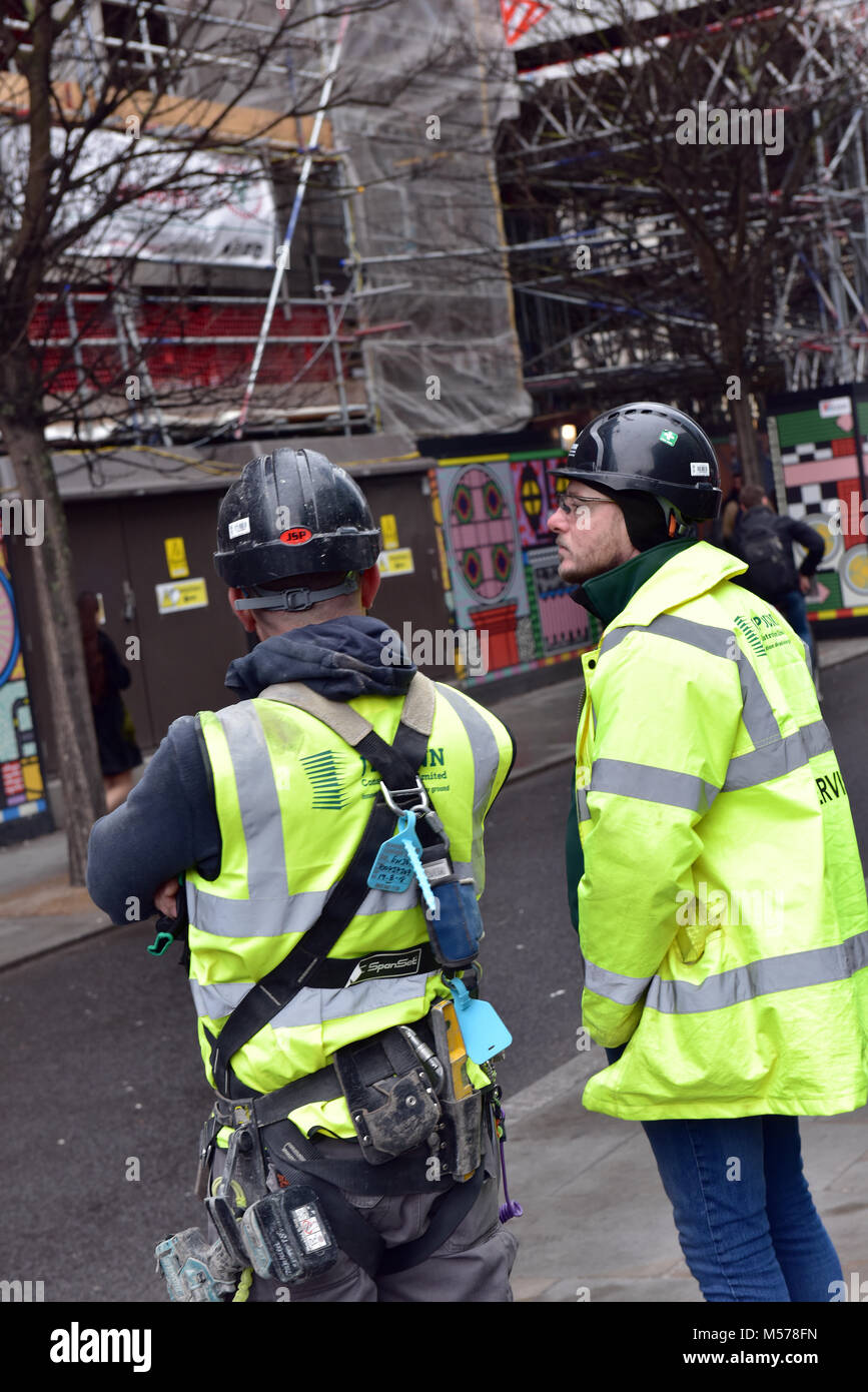 construction workers wearing high visibility jackets and hard hats or safety helmets and harnesses talking or discussing a job at the building sites. Stock Photo
