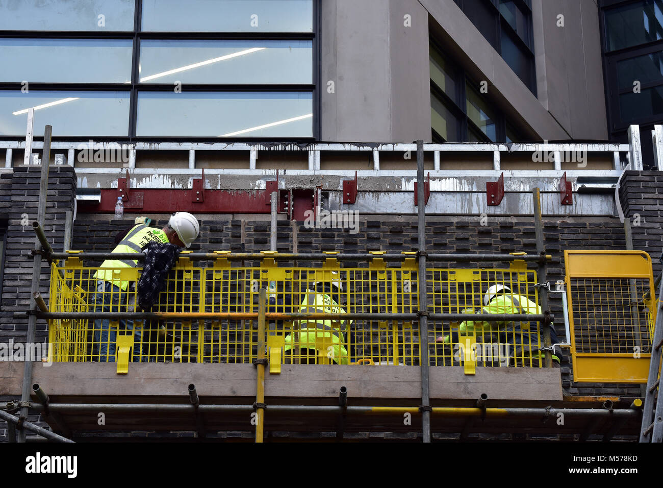 Construction workers werring high visibility clothing in a cradle or winch hoist cage fitting windows on a new build apartment block of offices london Stock Photo