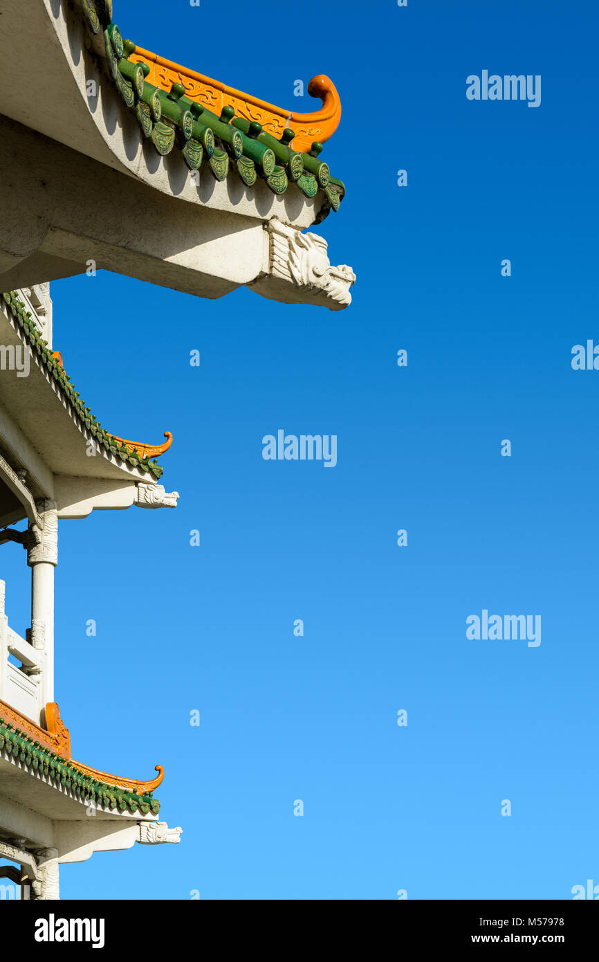 Chinese-inspired curved roof on a contemporary building with decorative glazed roof tiles and dragon shaped concrete beam against a deep blue sky. Stock Photo