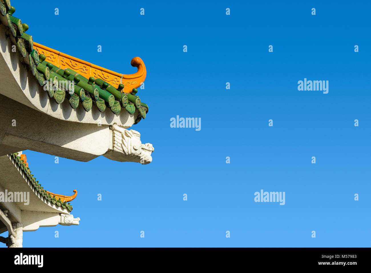 Chinese-inspired curved roof on a contemporary building with decorative glazed roof tiles and dragon shaped concrete beam against a deep blue sky. Stock Photo