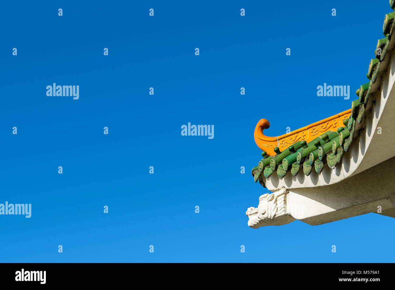 Chinese-inspired curved roof on a contemporary building with decorative glazed roof tiles and dragon shaped concrete beam against a deep blue sky. Stock Photo
