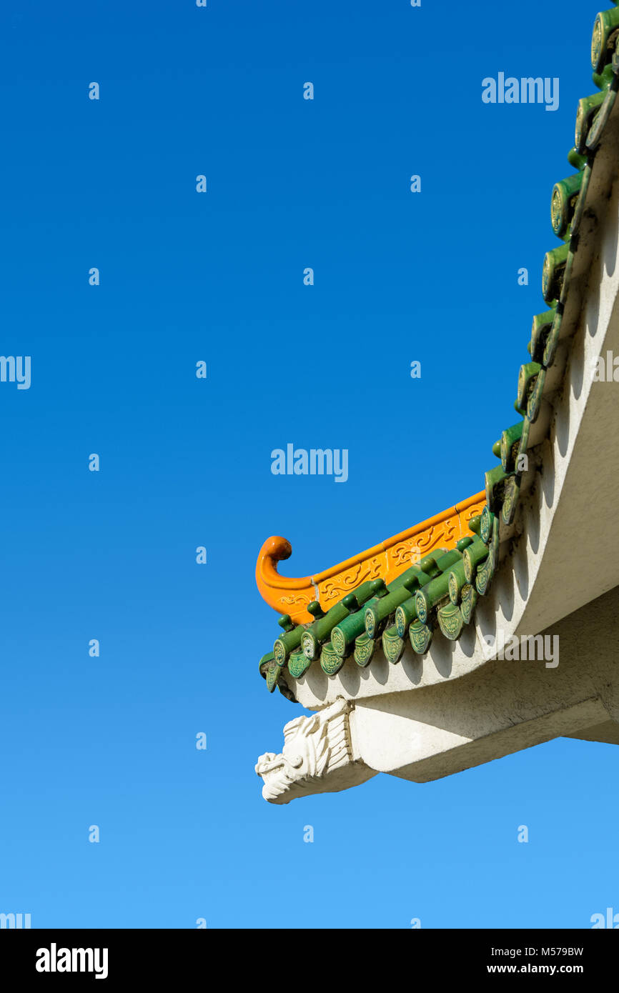Chinese-inspired curved roof on a contemporary building with decorative glazed roof tiles and dragon shaped concrete beam against a deep blue sky. Stock Photo