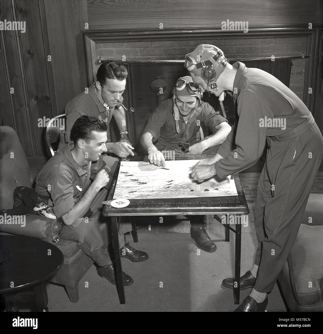 1942, USA, historical, four servicemen of the United States Army Air Forces (USAAF) wearing their flying kit sitting in a lounge playing the new board game, 'Air Combat Trainer'. Produced in conjunction with the US War Department, the game was a test of skill at combat flying, using miniatures of war planes and combat manoeuvres. Stock Photo
