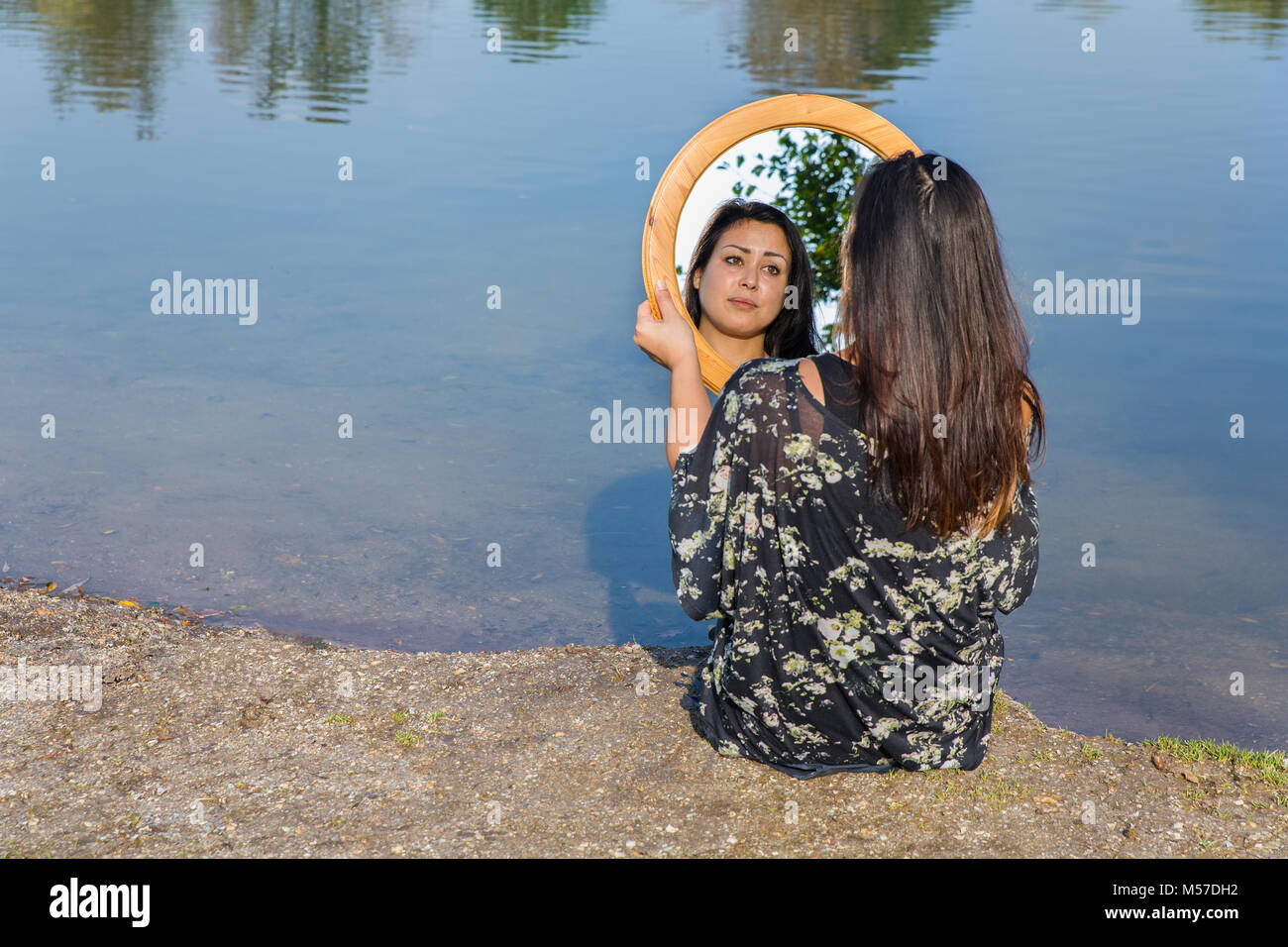 Woman looking in mirror at water Stock Photo