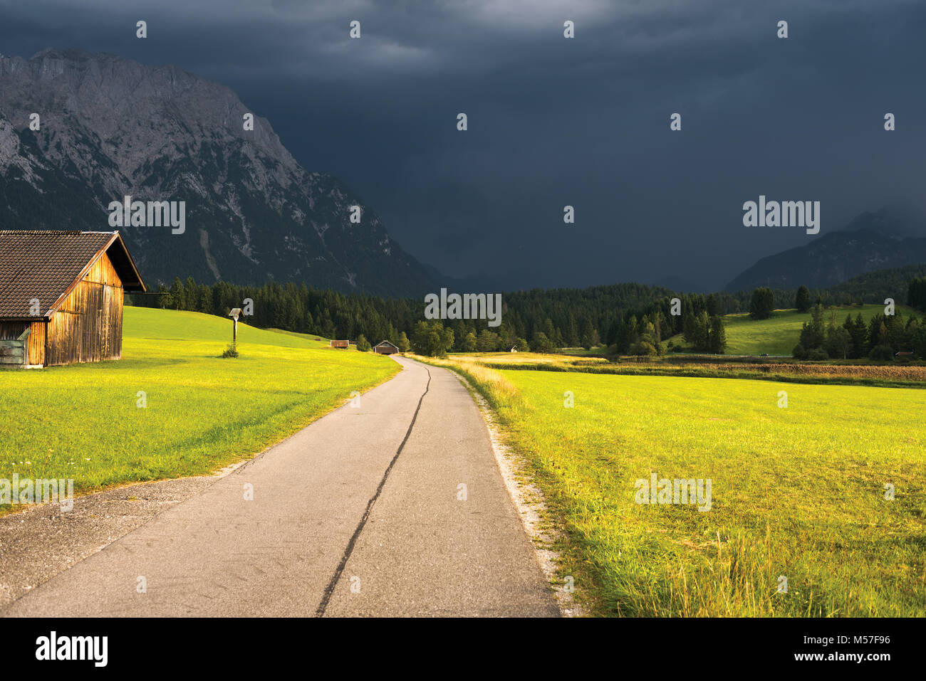 Smooth turning country road in alpine valley, thunderstorm Stock Photo