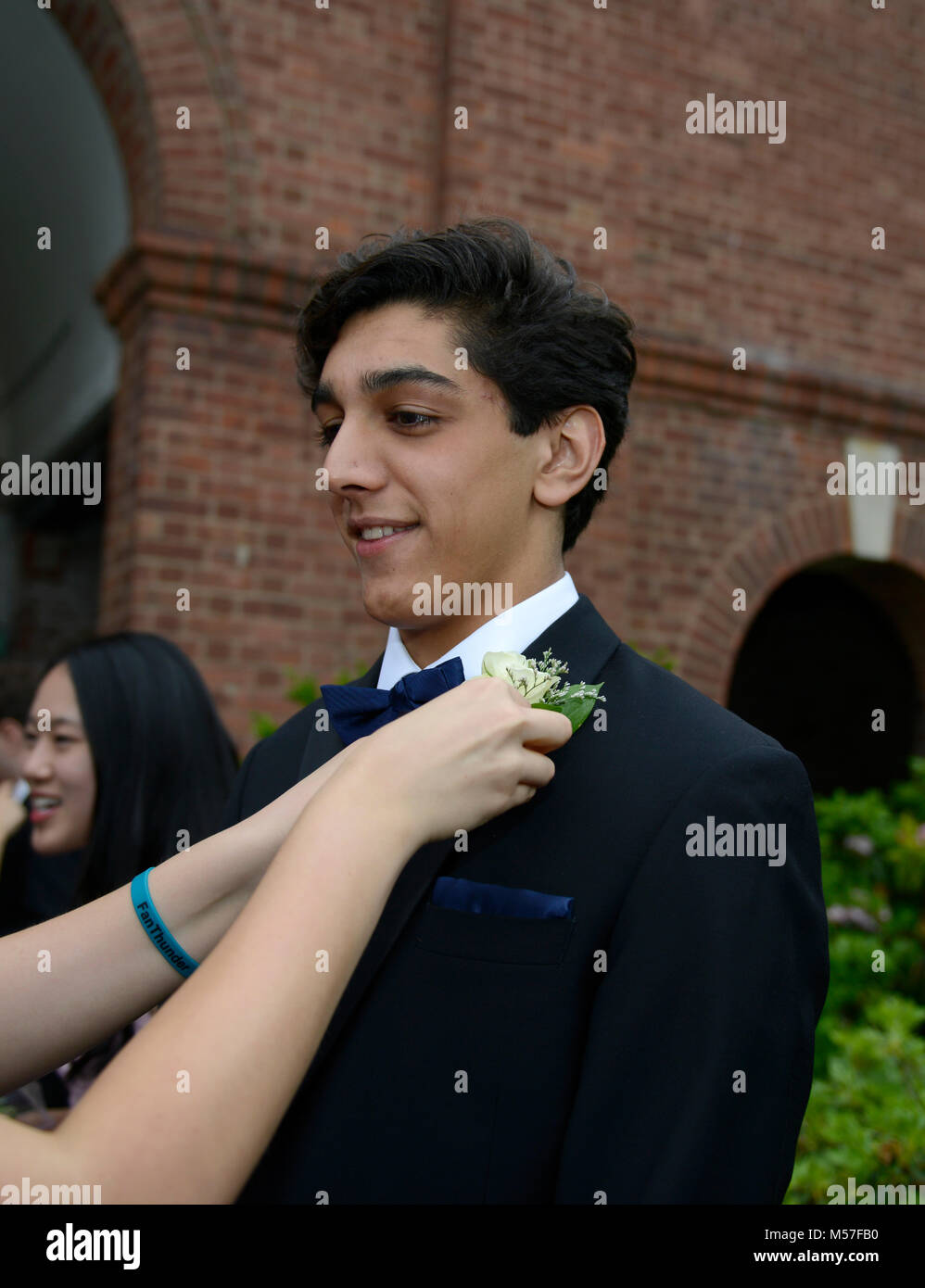 17 year old Indian American high school junior lets his prom date pin his boutonniere on his lapel Stock Photo