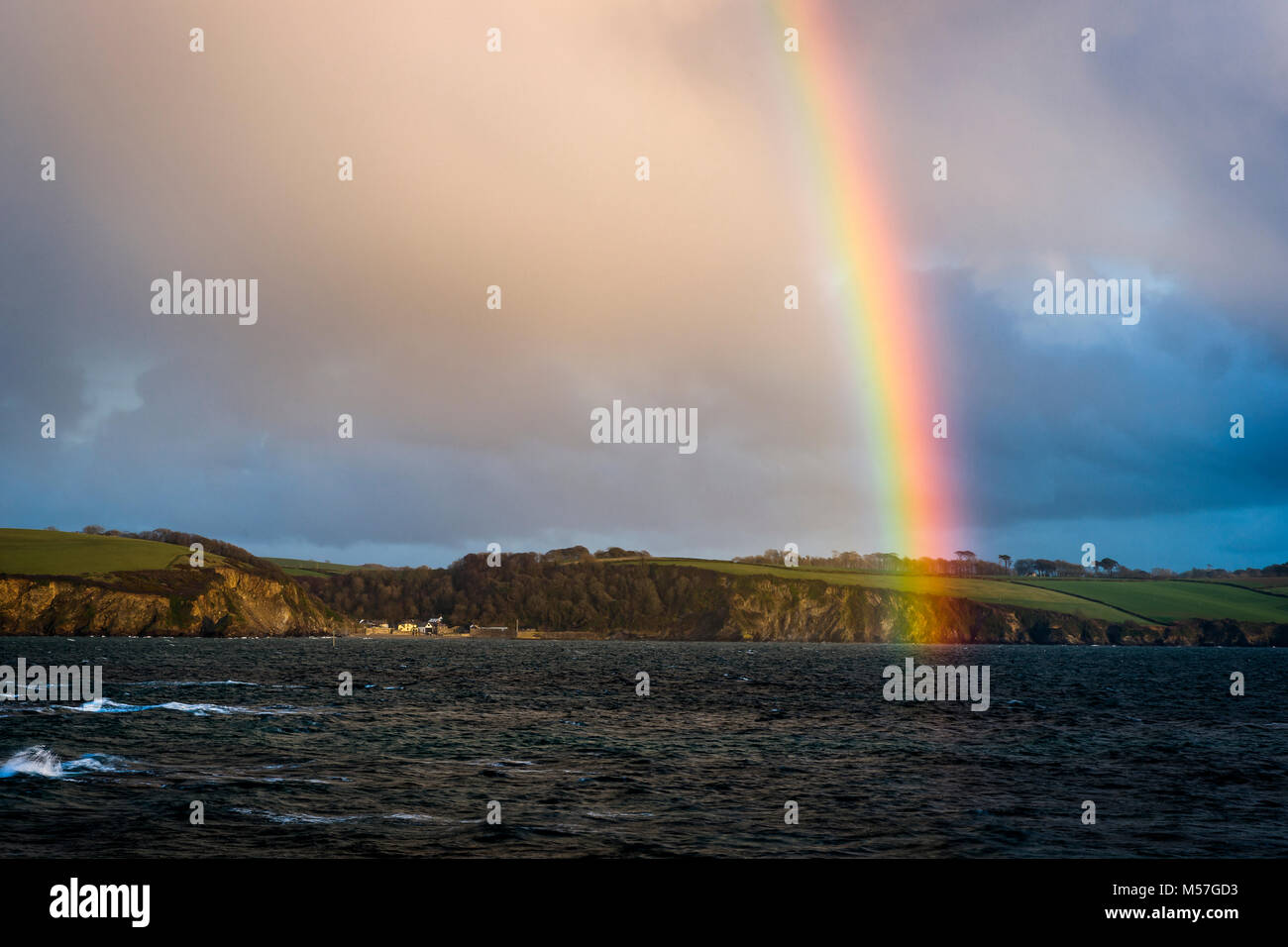 A vibrant rainbow arches across St Austell Bay  and the small coastal town of Polkerris in Cornwall Stock Photo
