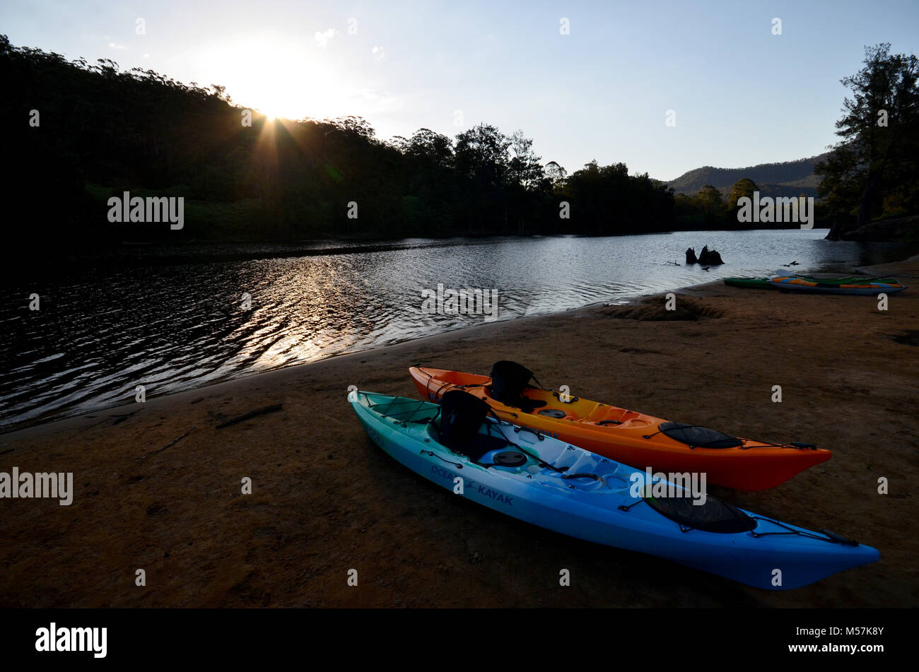 Kayaks by the waters edge with sun going down behind the trees, taken at Kangaroo Valley NSW Australia Stock Photo
