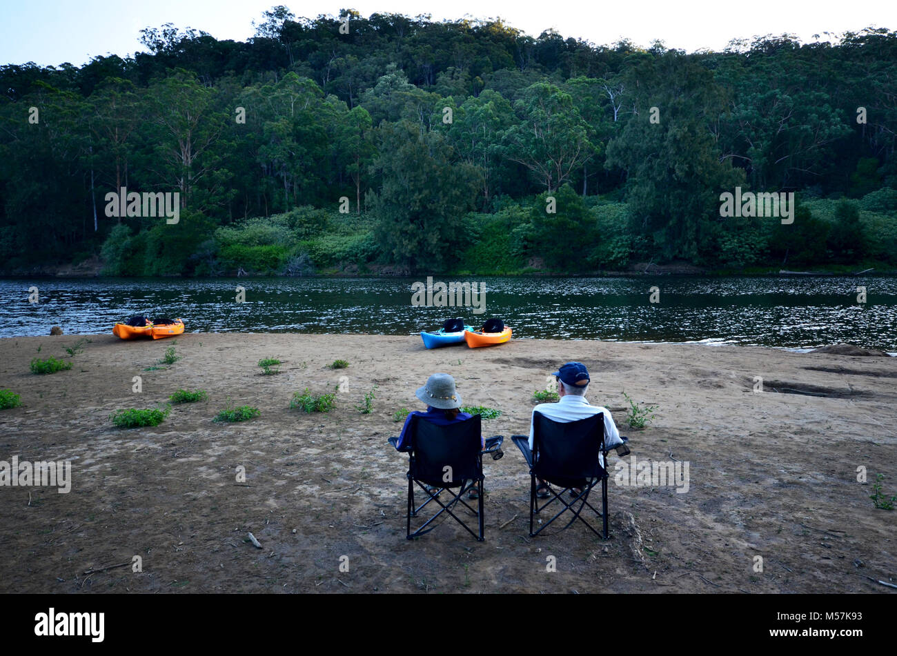 Isolation. Two people sitting in camping chairs by the river at Kangaroo Valley with Kayaks in the background Stock Photo