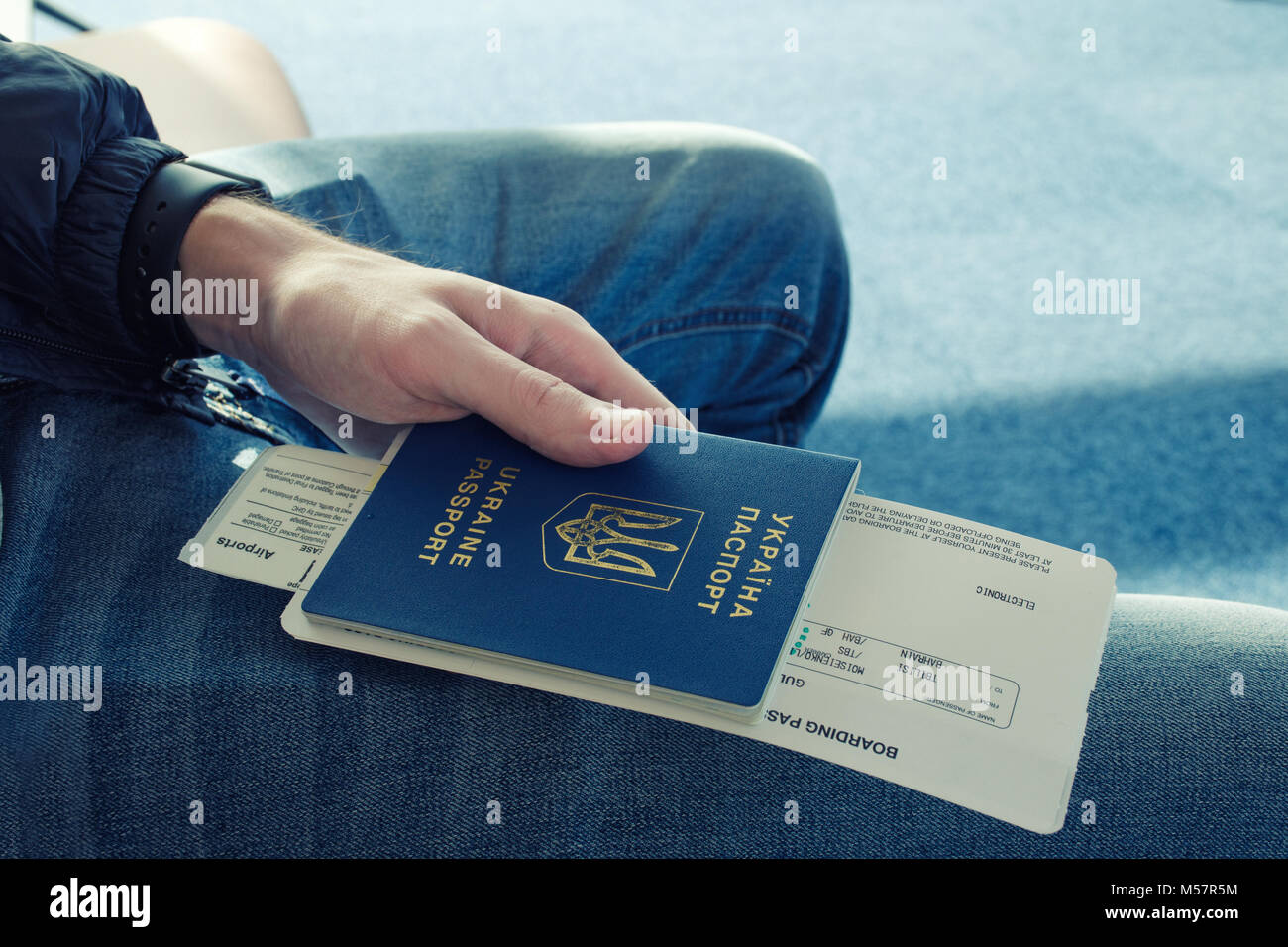 Young men in jeans holding in hand foreign passport of Ukraine with airplane ticket attached to it. Stock Photo