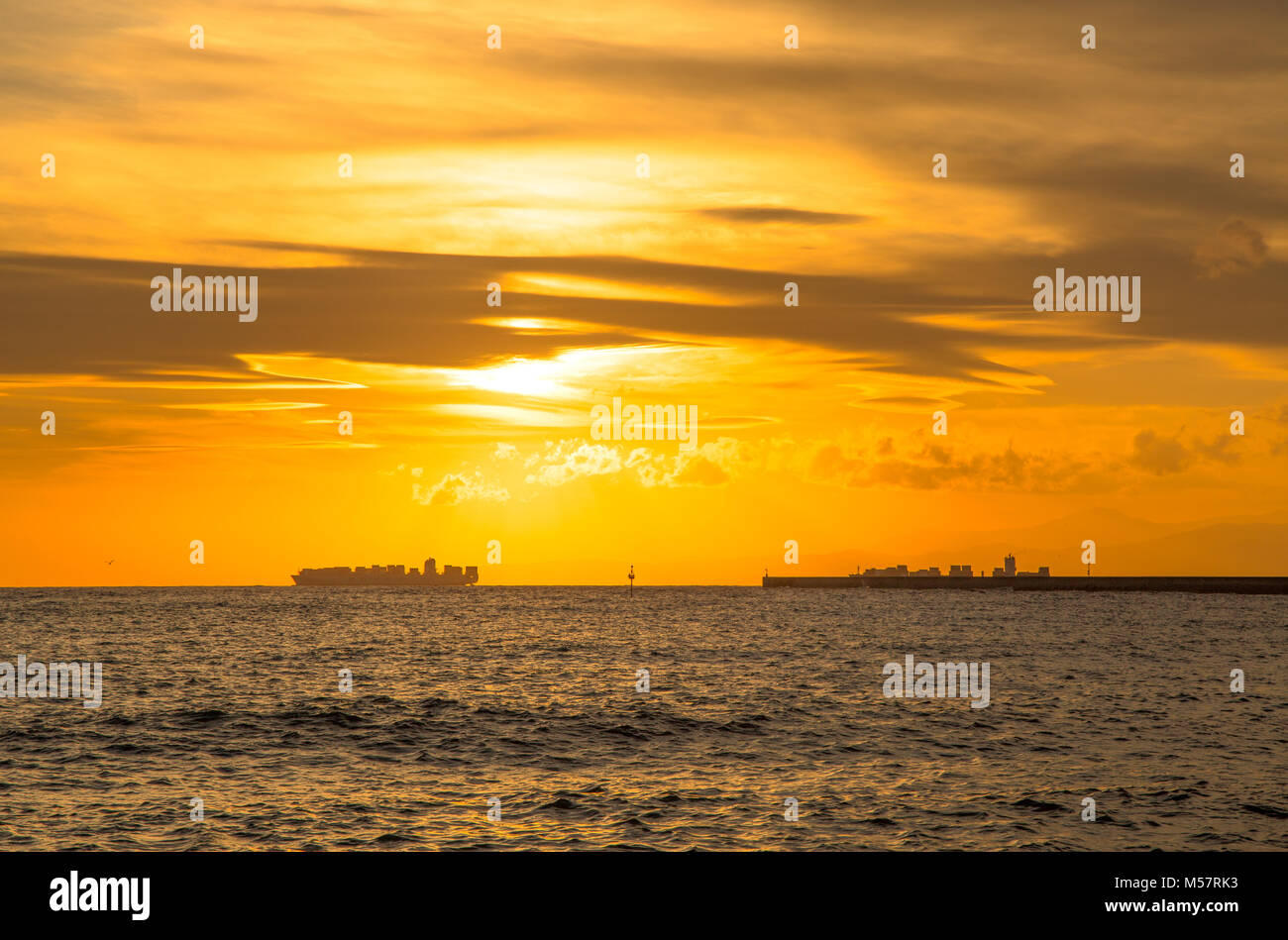 Container ship on the horizon and the pier at sunset Stock Photo - Alamy