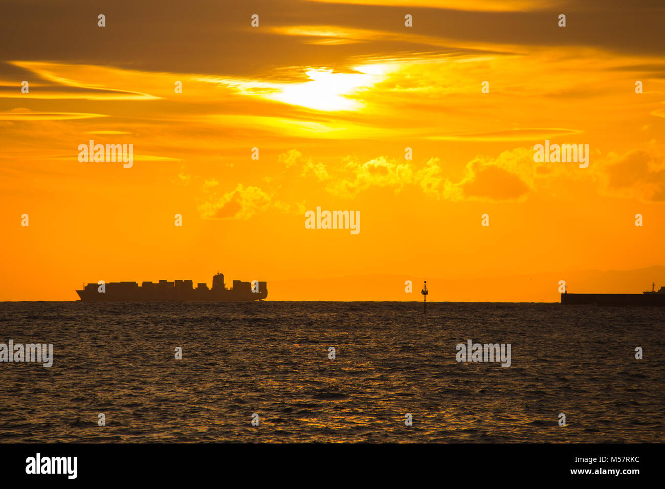 Container ship on the horizon and the pier at sunset Stock Photo - Alamy