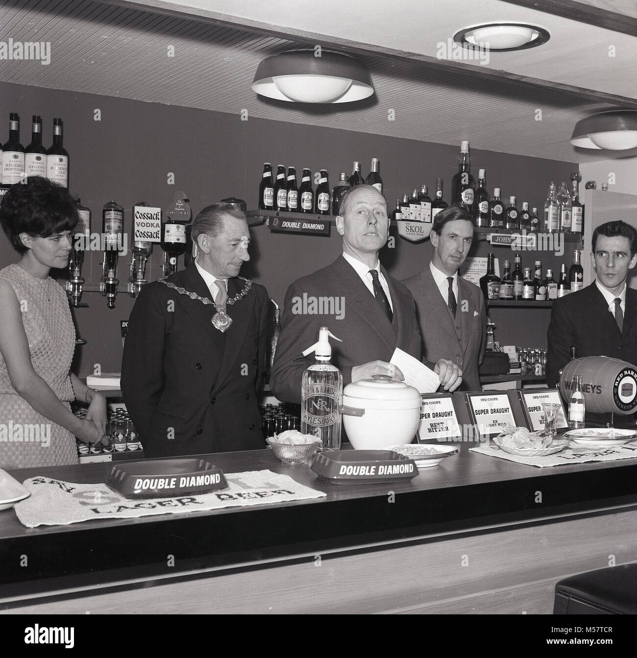 1965, historical picture showing the mayor and local dignitaries officially opening the community pub, The John Kennedy, named after the famous American President, JFK, at Meadowcroft housing estate in Aylesbury, Bucks, England, UK. In view, are all the great British beer brands of the era including 'Double Diamond', Skol and Watneys 'Red Barrel'. Stock Photo