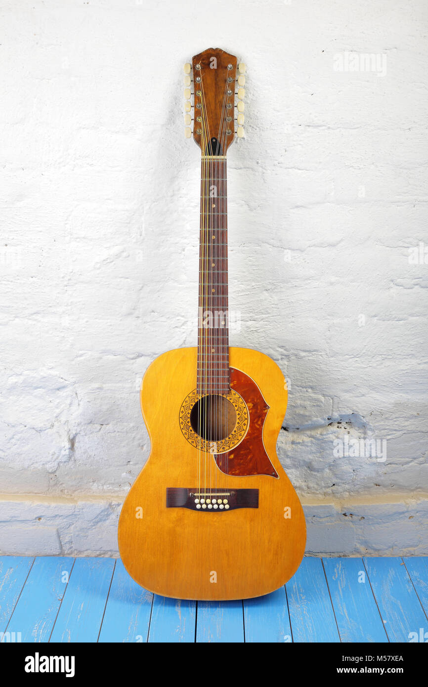 Musical instrument - Front view vintage twelve-string acoustic guitar on a brick background and blue wooden floor. Stock Photo