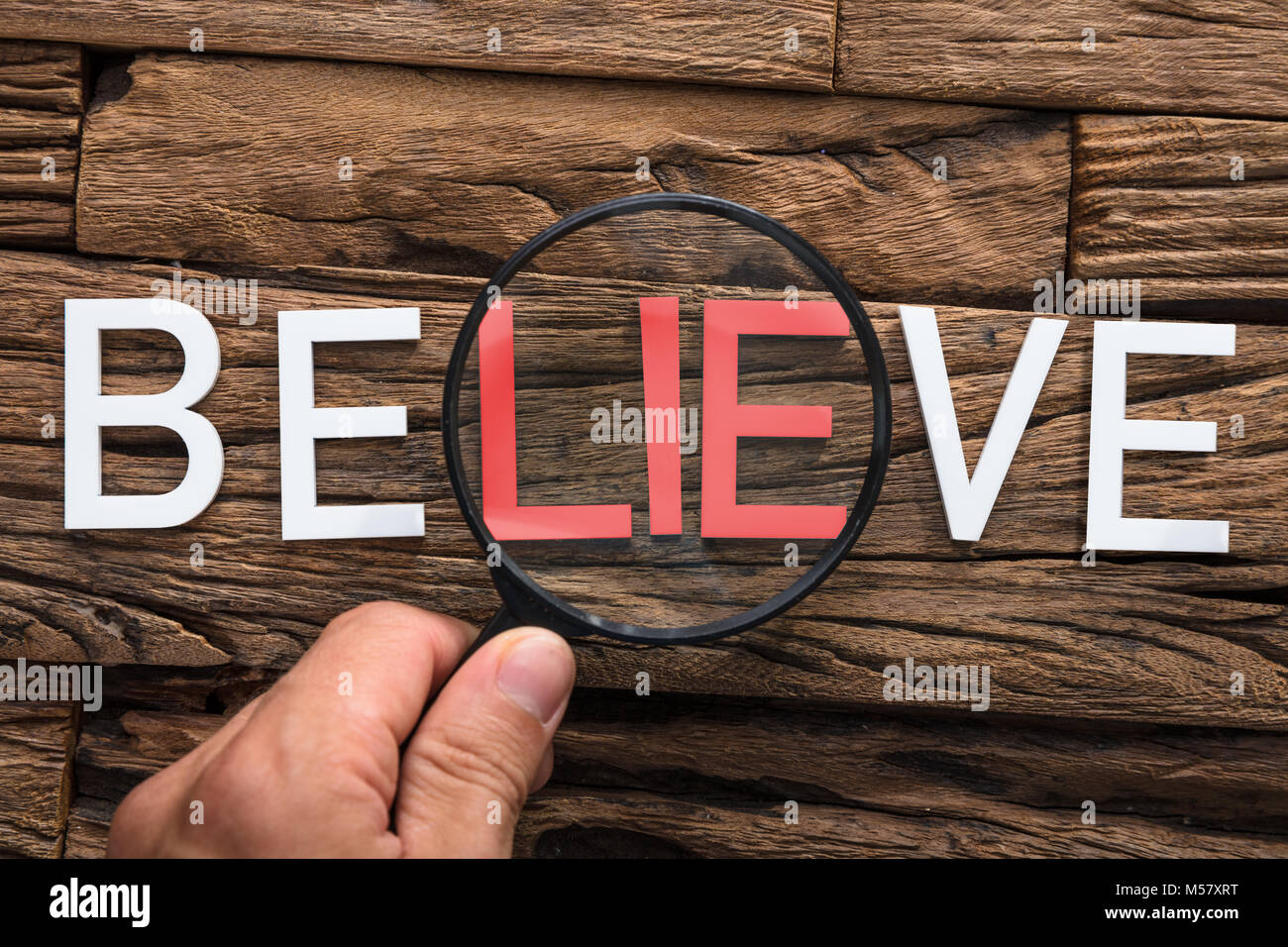 Closeup of hand holding magnifying glass over word lie in believe on wood Stock Photo