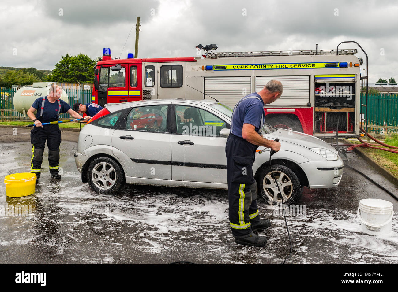 Members of Skibbereen Fire Brigade wash a car as part of a charity car wash in Skibbereen Fire Station, County Cork, Ireland with copy space. Stock Photo
